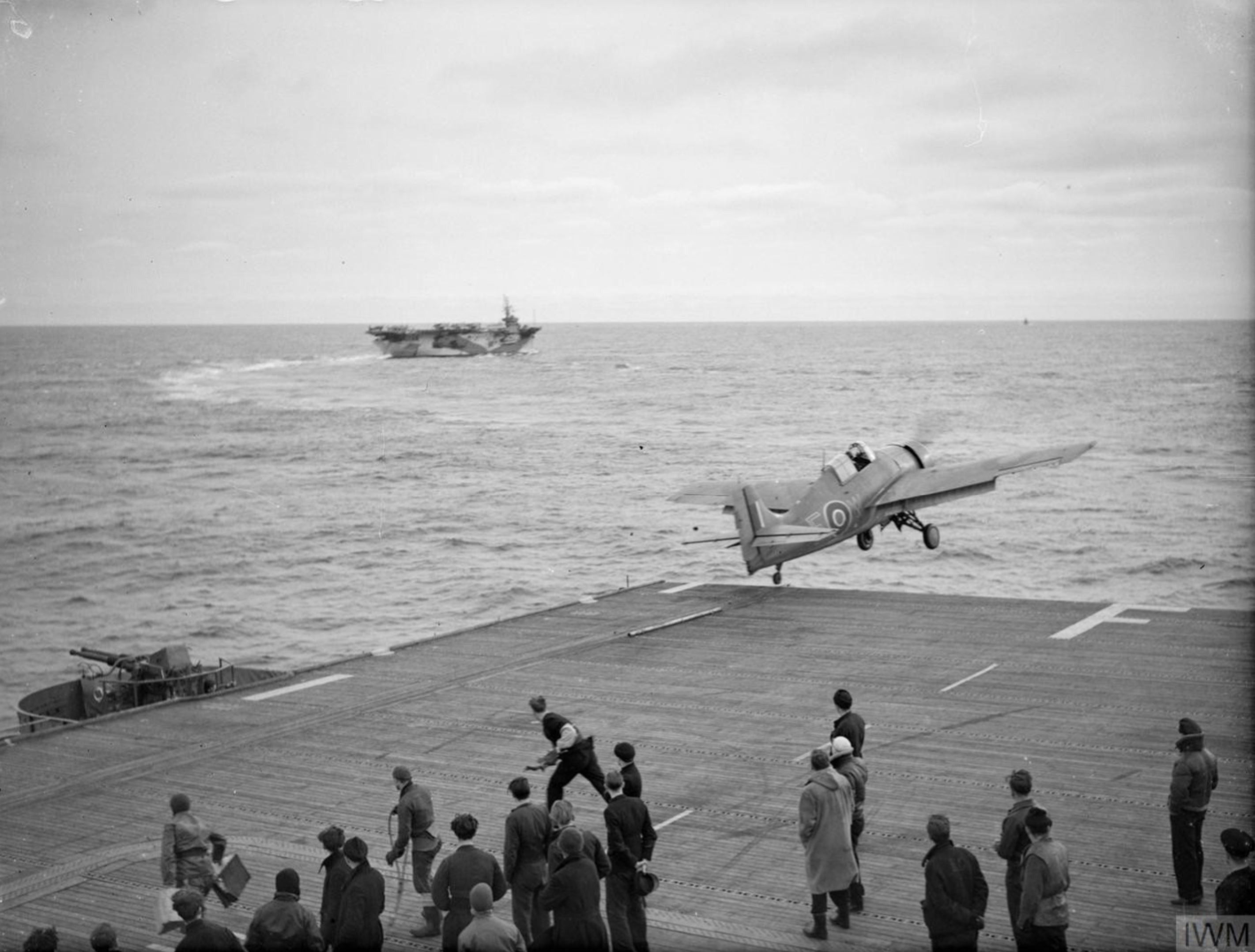 Fleet Air Arm Martlet MkII EW catapulted from HMS Fencer with HMS Trumpeter background Oct 1944 IWM A26134